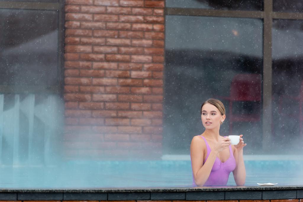 young woman holding cup of coffee in outdoor swimming pool  - Foto, afbeelding