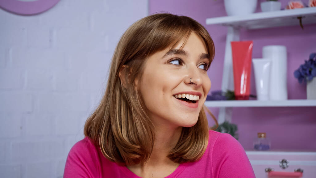 Ευτυχισμένη νεαρή γυναίκα με διαπεραστικό χαμόγελο, ενώ κοιτάζει μακριά στο σπίτι - Φωτογραφία, εικόνα