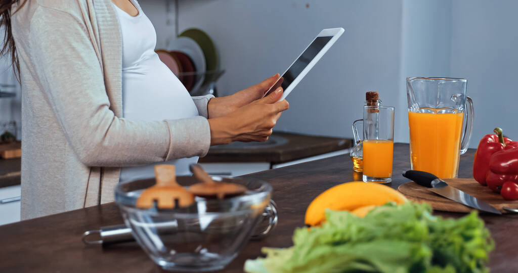 Обрезанный вид беременной женщины с цифровыми таблетками рядом со свежей пищей  - Фото, изображение