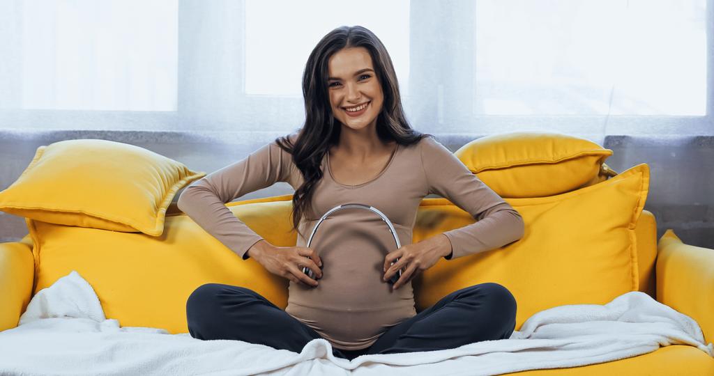 Vidám terhes nő kezében fejhallgató közel has  - Fotó, kép
