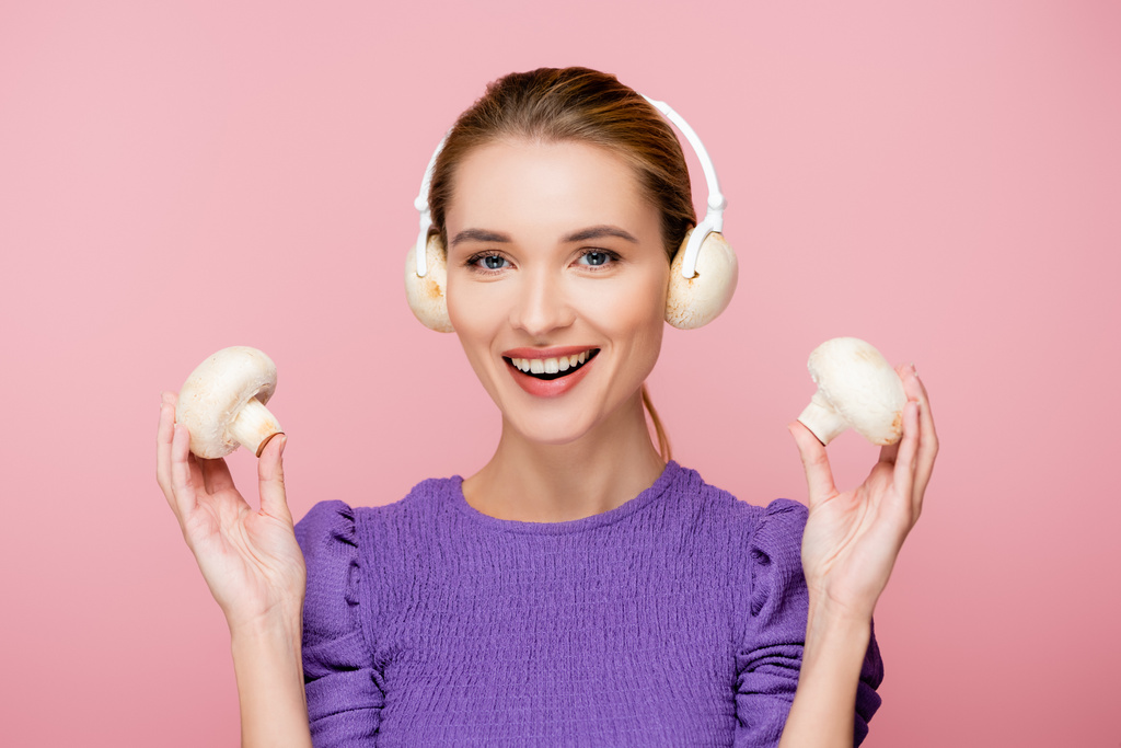 smiling woman with mushrooms in headphones holding champignons isolated on pink - Photo, Image