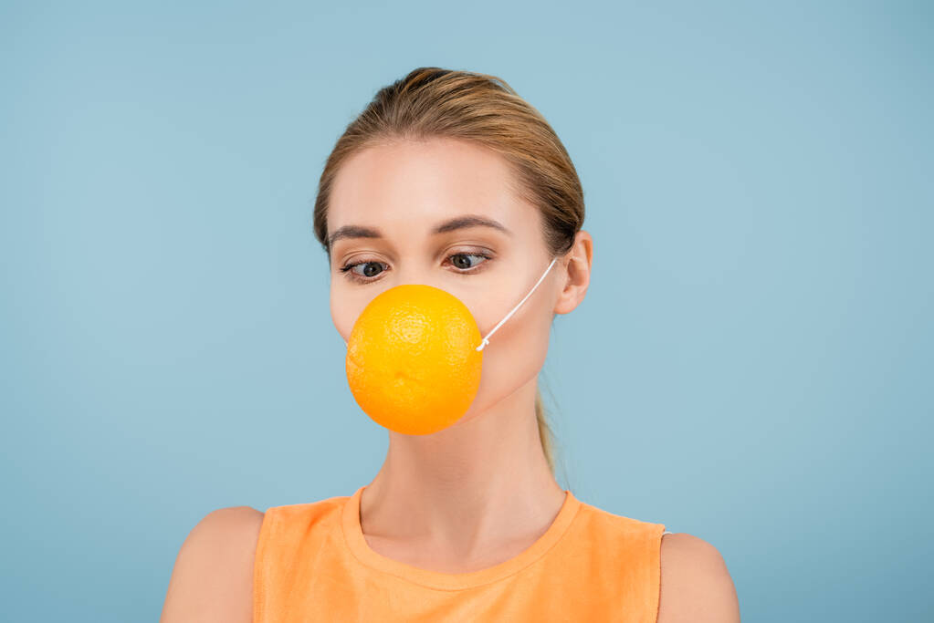 mujer joven en máscara de seguridad hecha de naranja medio aislado en azul - Foto, Imagen
