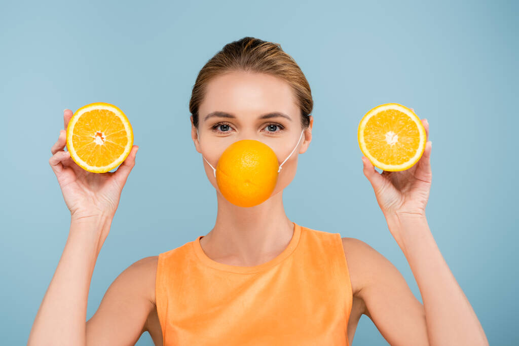 mujer joven en máscara de protección hecha de naranja mirando a la cámara aislada en azul - Foto, Imagen