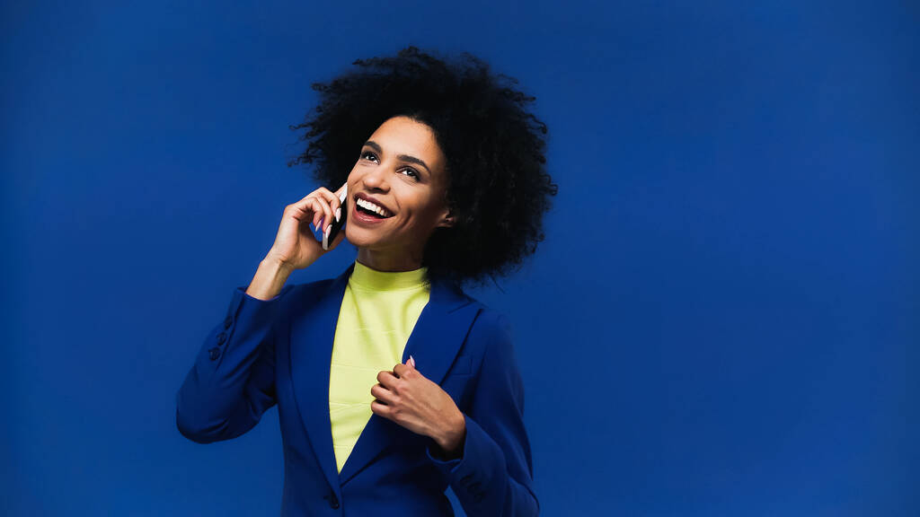Веселая африканская американка разговаривает на смартфоне, изолированном на голубом  - Фото, изображение