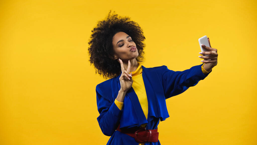 Mujer afroamericana mostrando signo de paz durante selfie aislado en amarillo - Foto, Imagen