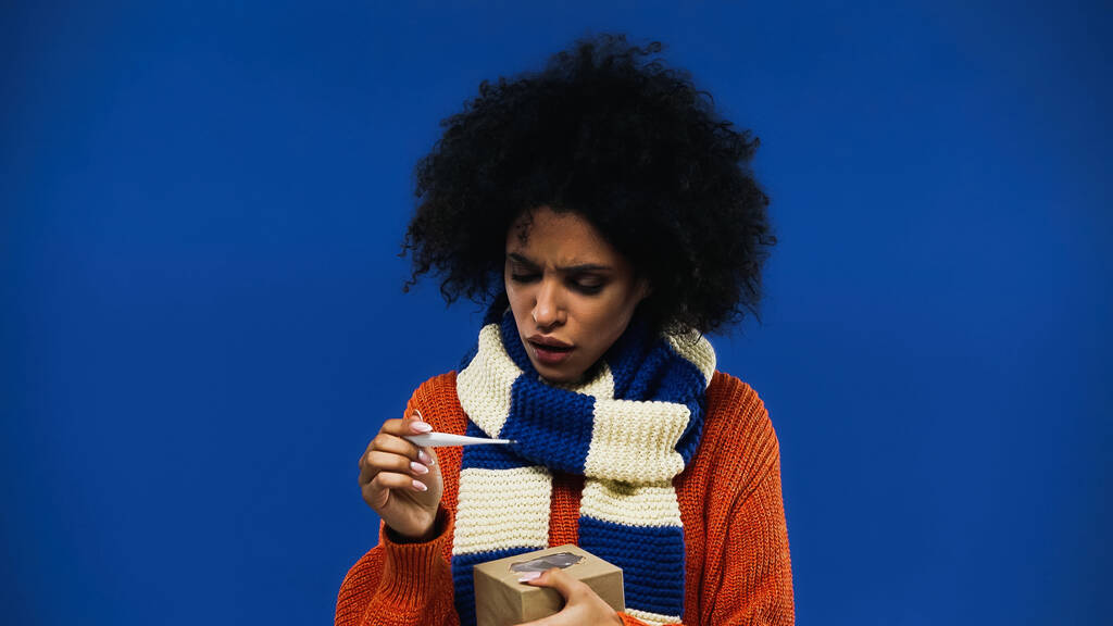 Ill femme afro-américaine tenant thermomètre et boîte isolée sur bleu  - Photo, image