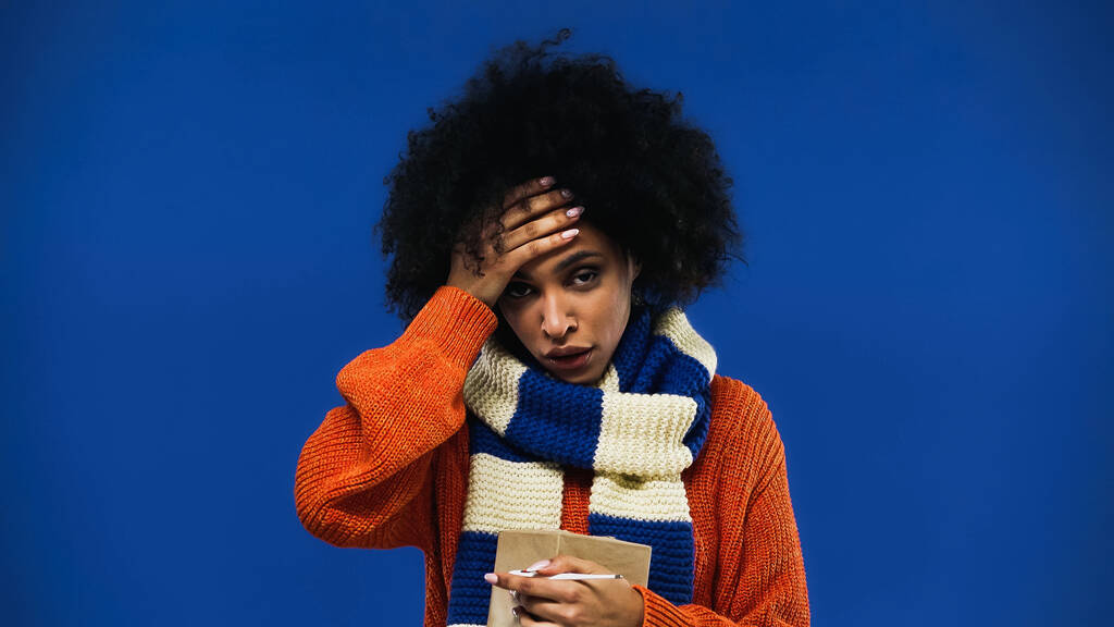 Femme afro-américaine malade tenant thermomètre isolé sur bleu  - Photo, image