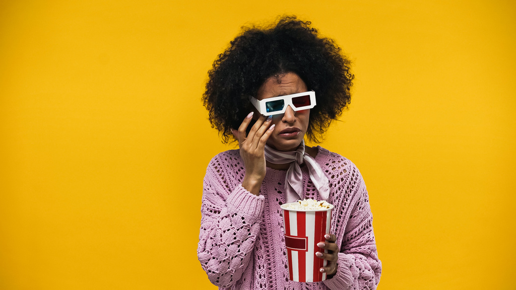 Upset african american woman in 3d glasses crying and holding popcorn isolated on yellow - Photo, Image