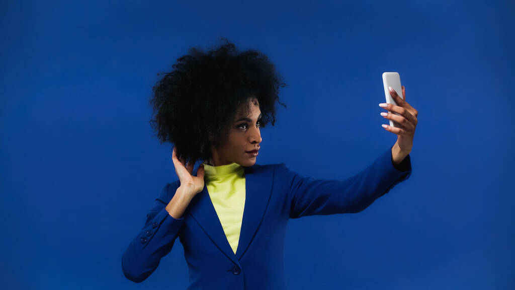 Femme afro-américaine prenant selfie avec smartphone isolé sur bleu - Photo, image