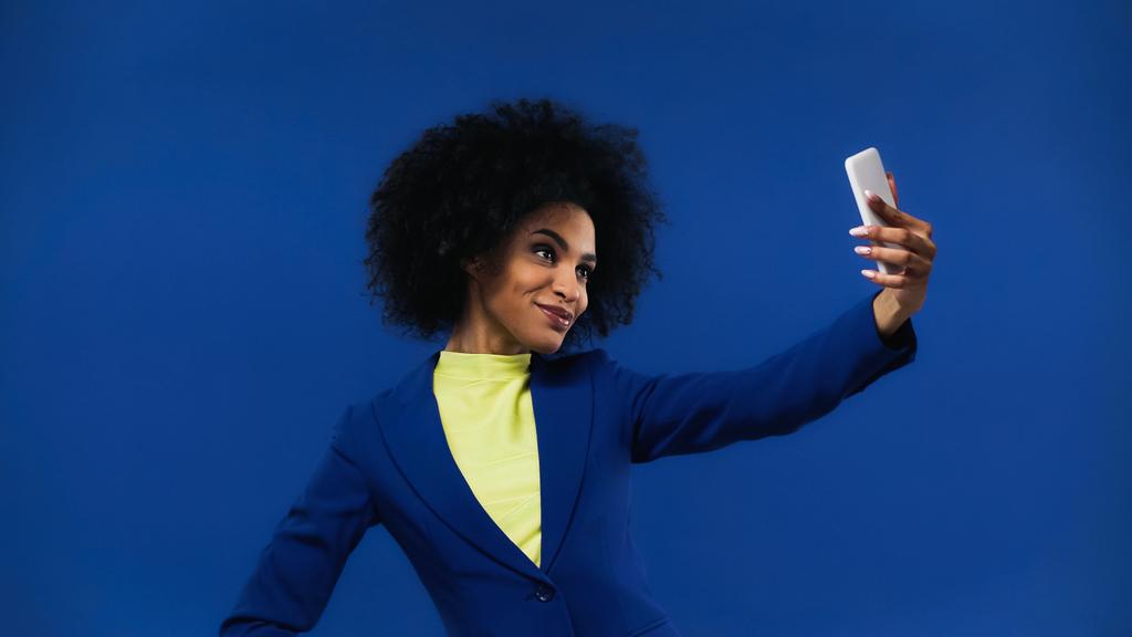 Sorridente donna afro-americana scattare selfie isolato su blu - Foto, immagini
