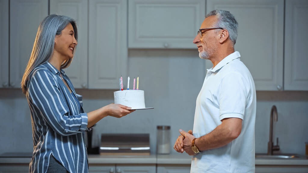 πλαϊνή άποψη της ηλικιωμένης Ασιάτισσας που δίνει τούρτα γενεθλίων στον ευτυχισμένο σύζυγο - Φωτογραφία, εικόνα
