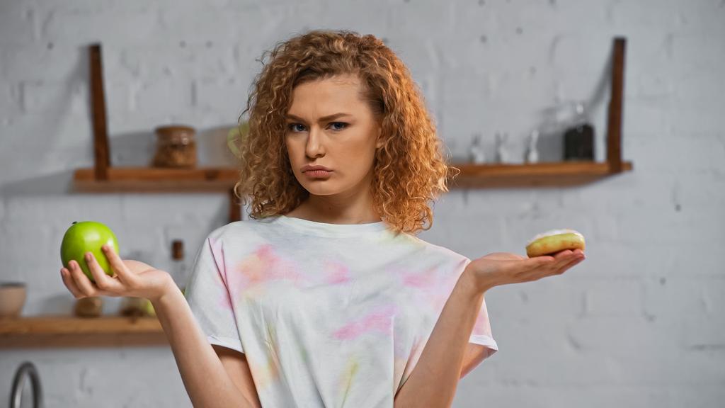 curly young woman choosing between apple  and donut - Photo, Image