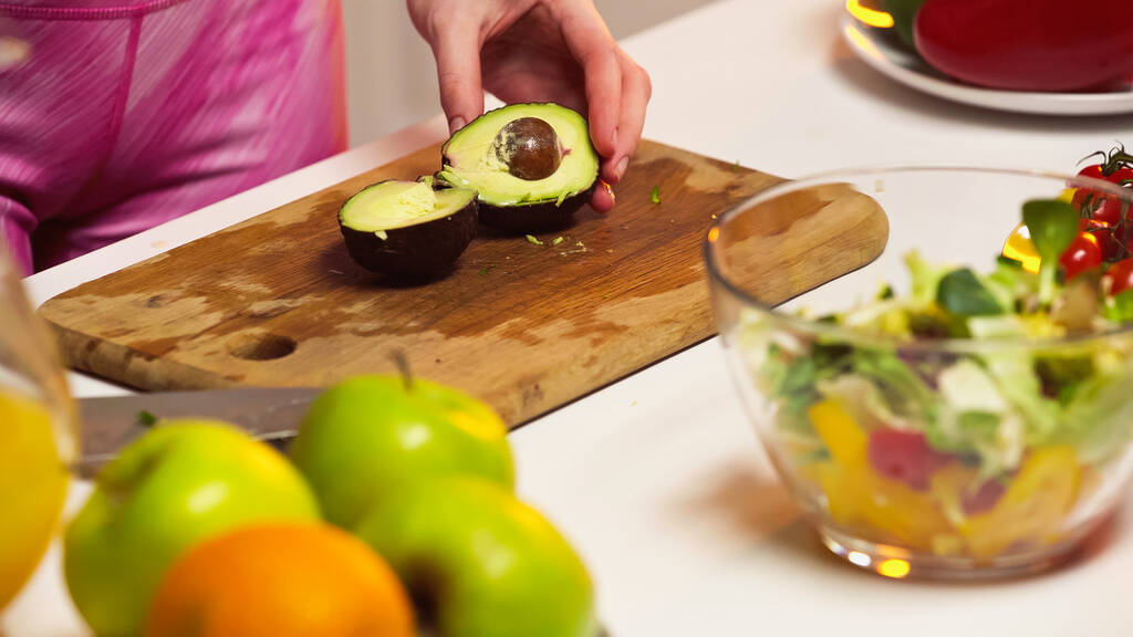 bijgesneden weergave van vrouw in de buurt avocado helften op snijplank - Foto, afbeelding
