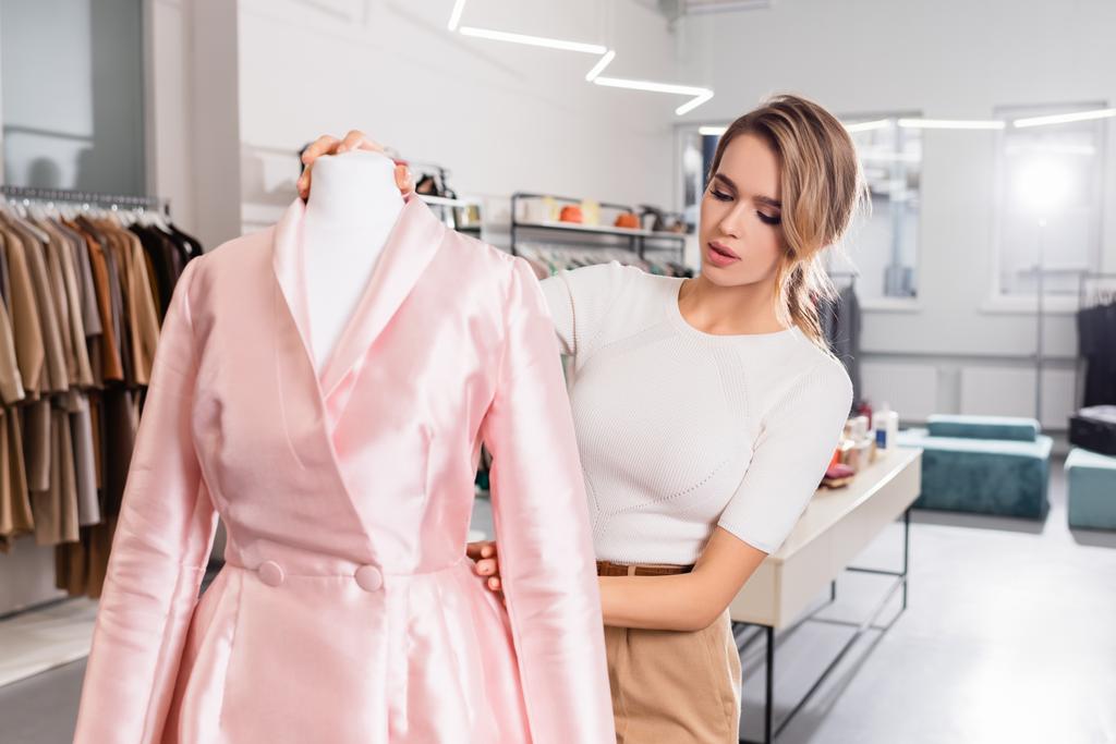 Hübsche Verkäuferin trägt rosa Mantel auf Schaufensterpuppe im Showroom  - Foto, Bild