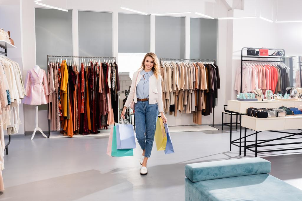 Stylische Frau lächelt, während sie im Showroom Einkaufstüten hält  - Foto, Bild