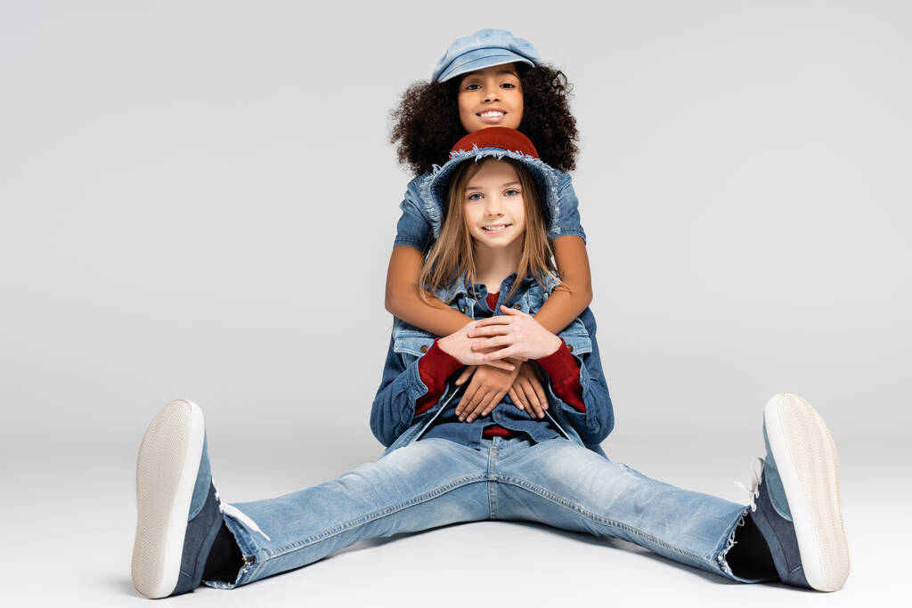 щаслива афроамериканська дівчина обіймає веселого, модного друга, що сидить на сірому
 - Фото, зображення