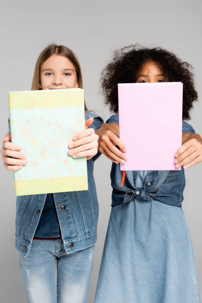 πολυπολιτισμικές μαθήτριες με denim ρούχα που κρατούν βιβλία απομονωμένα σε γκρι χρώμα - Φωτογραφία, εικόνα