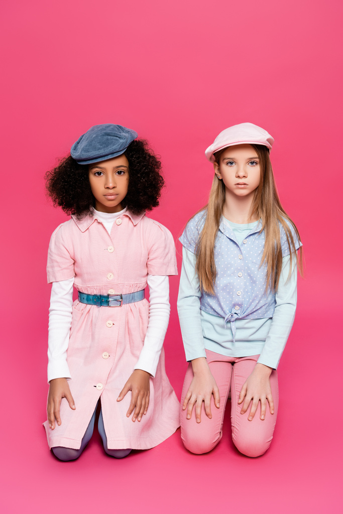 multikulturális lányok divatos ruhákban és sapkákban, akik rózsaszín pózban nézik a kamerát - Fotó, kép