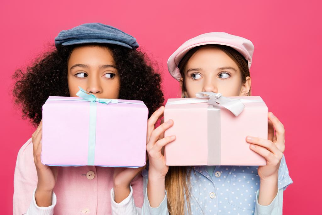 Модные межрасовые девушки в модных шапках держат подарки изолированы на розовый - Фото, изображение