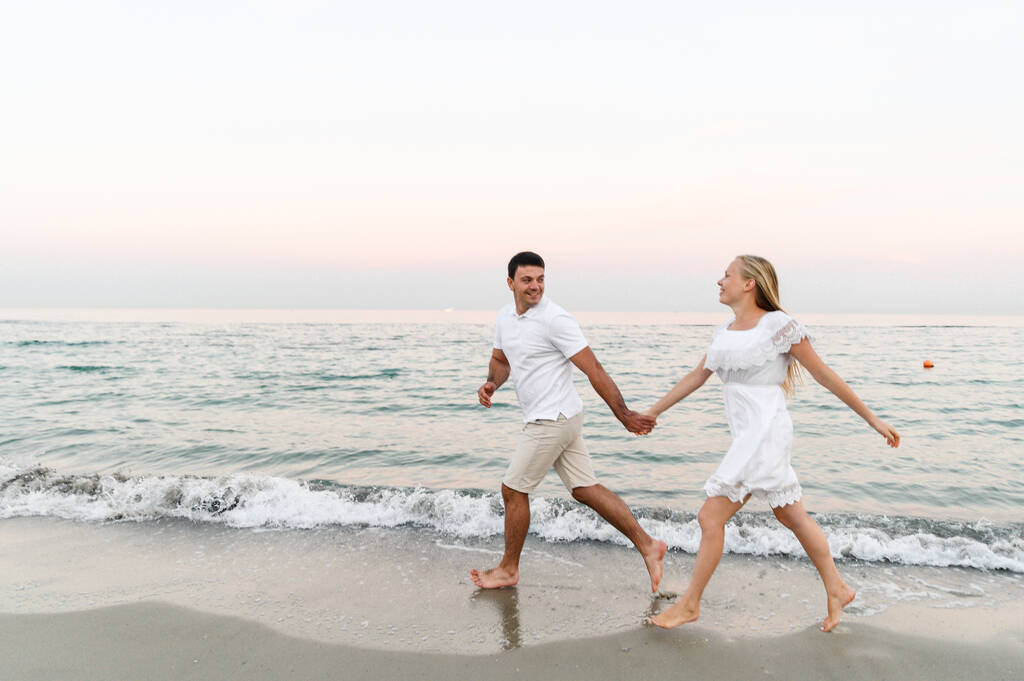 Парень в летней одежде ходит по океану. муж и жена на романтическом закате дня у моря. любовники бегают по пляжу. Медовый месяц для молодоженов. - Фото, изображение