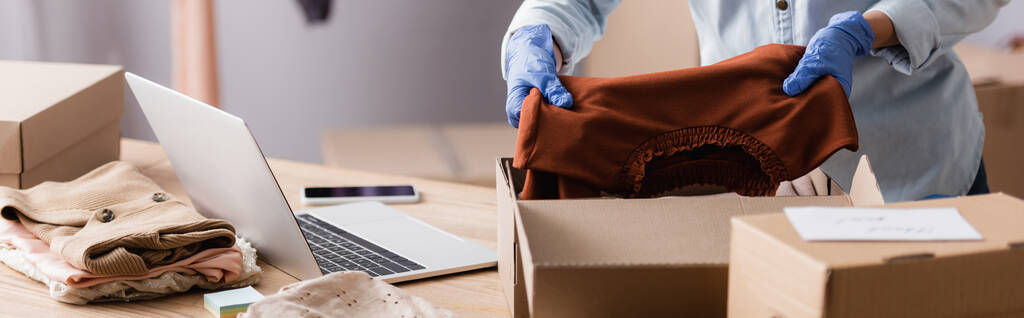partial view of showroom owner in latex gloves packing clothes into boxes, banner - Photo, Image