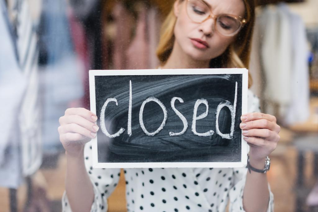 Empresaria disgustada sosteniendo el tablero con letras cerradas en la sala de exposición, fondo borroso - Foto, imagen