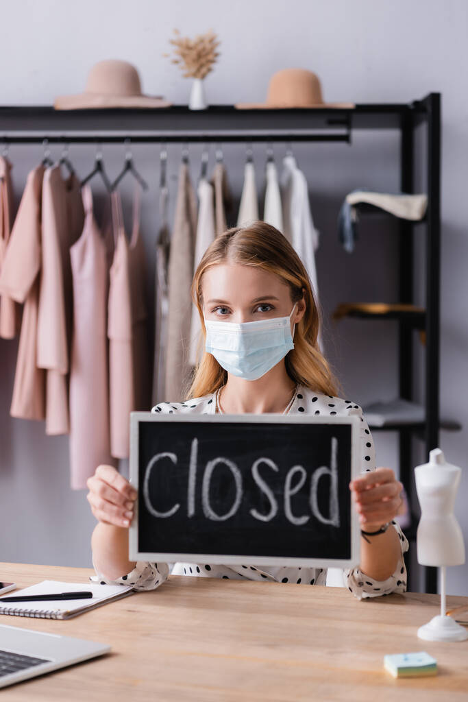 majitel showroomu sedí na pracovišti v lékařské masce a drží deska s uzavřeným nápisem - Fotografie, Obrázek