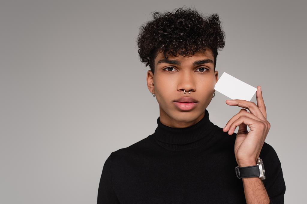 τρυπημένος Αφροαμερικάνος με ζιβάγκο πουλόβερ κρατώντας λευκή κάρτα απομονωμένη σε γκρι - Φωτογραφία, εικόνα