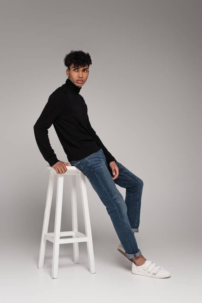 アフリカ系アメリカ人の若者の完全な長さですタートルネックセーターで白い椅子にもたれてグレー - 写真・画像