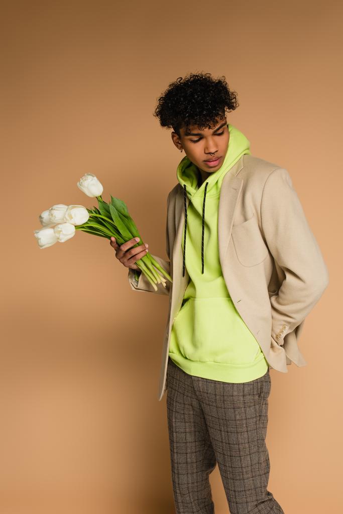 joven afroamericano hombre en verde sudadera con capucha y chaqueta con tulipanes en beige - Foto, imagen
