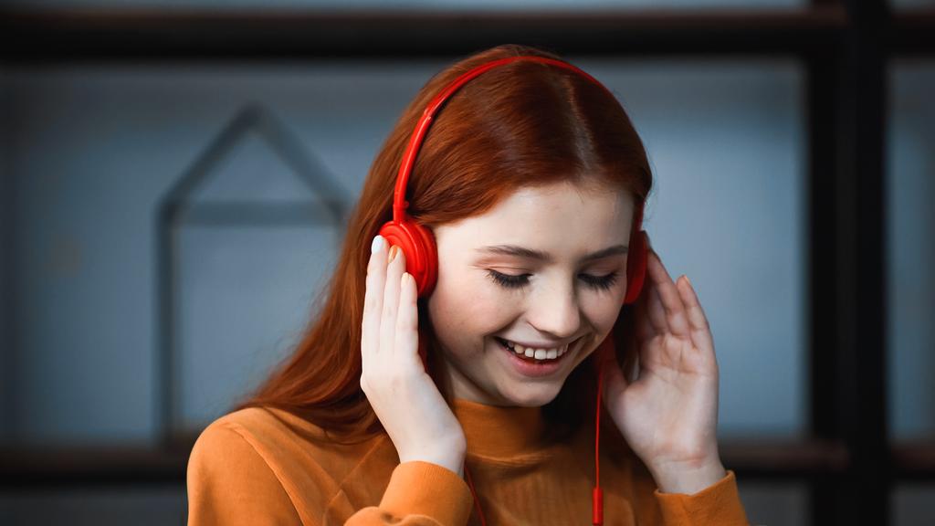 Χαμογελώντας κόκκινα μαλλιά κορίτσι χρησιμοποιώντας ακουστικά στο σπίτι  - Φωτογραφία, εικόνα