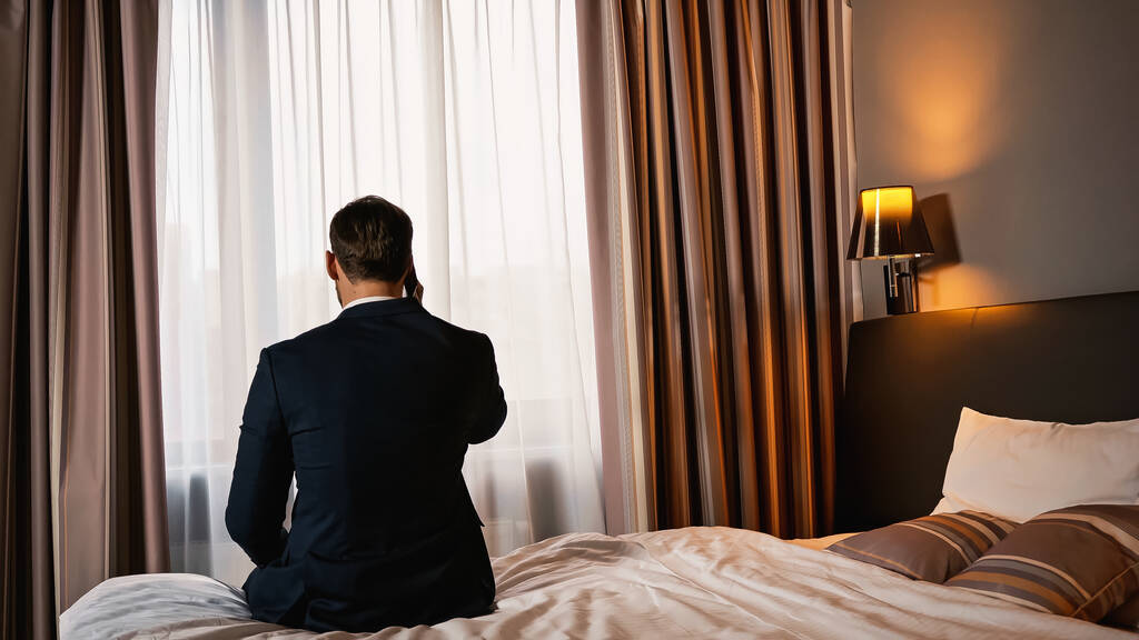 Visão traseira do homem de negócios falando no smartphone no quarto de hotel  - Foto, Imagem