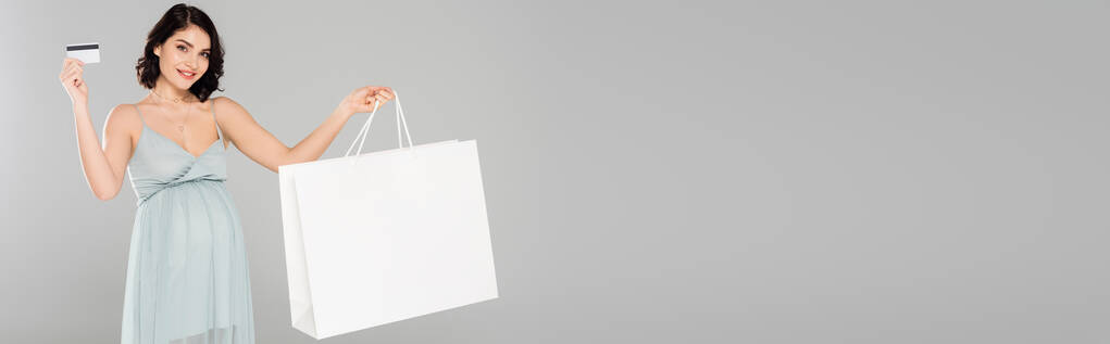 Uśmiechnięta kobieta w ciąży z torbą na zakupy i kartą kredytową na szarym, szarym banerze  - Zdjęcie, obraz