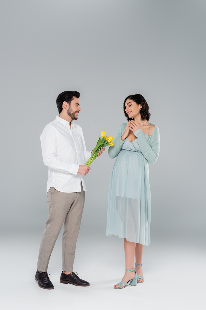 Hombre dando tulipanes a la esposa embarazada sobre fondo gris - Foto, Imagen