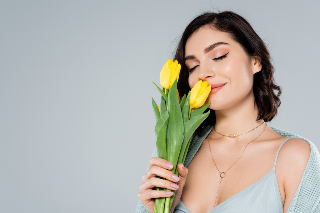 Молода жінка пахне жовтими тюльпанами ізольовані на сірому
  - Фото, зображення