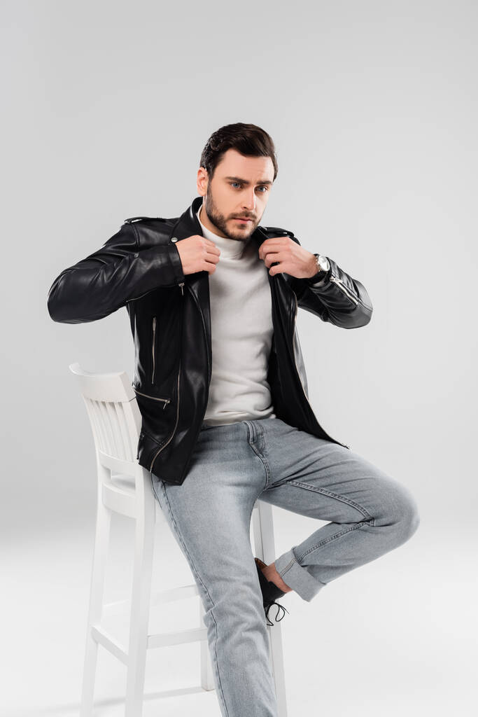 Homem elegante usando jaqueta de couro na cadeira no fundo cinza  - Foto, Imagem