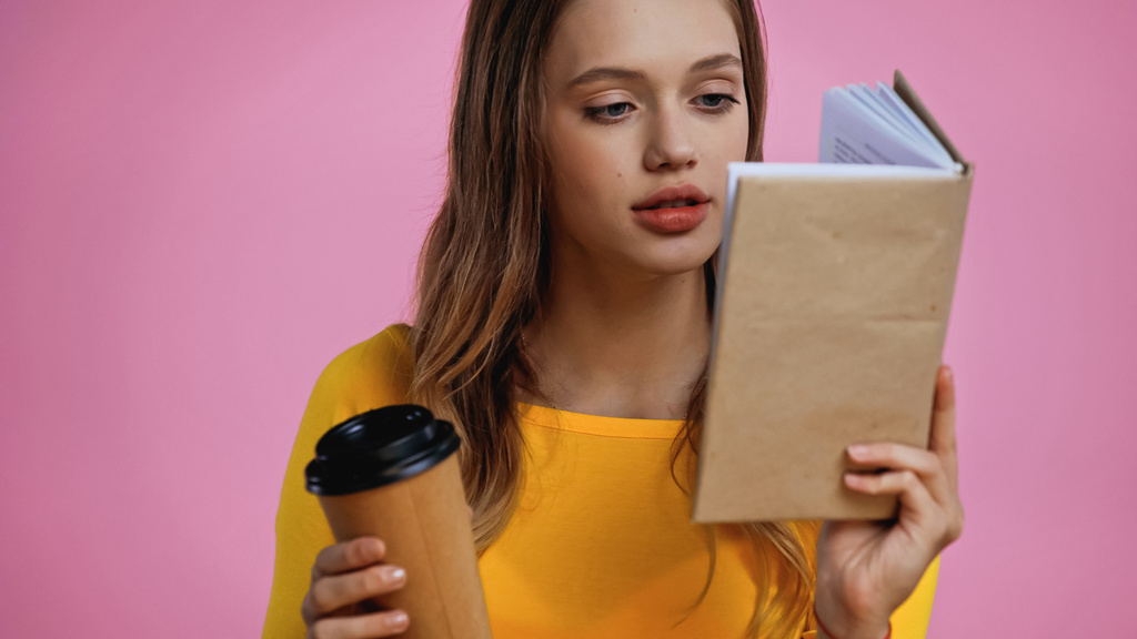 teenage girl reading book and holding coffee to go isolated on pink  - Photo, Image