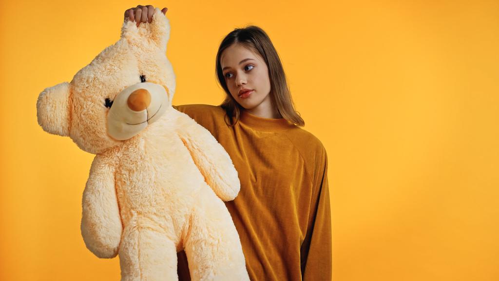 Unzufriedener Teenager im Pullover sieht Teddybär isoliert auf gelb - Foto, Bild