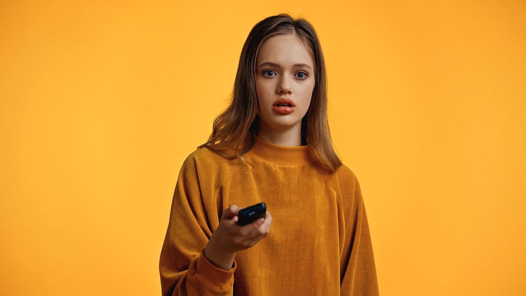 sorpreso adolescente in maglione tenendo telecomando isolato su giallo - Foto, immagini