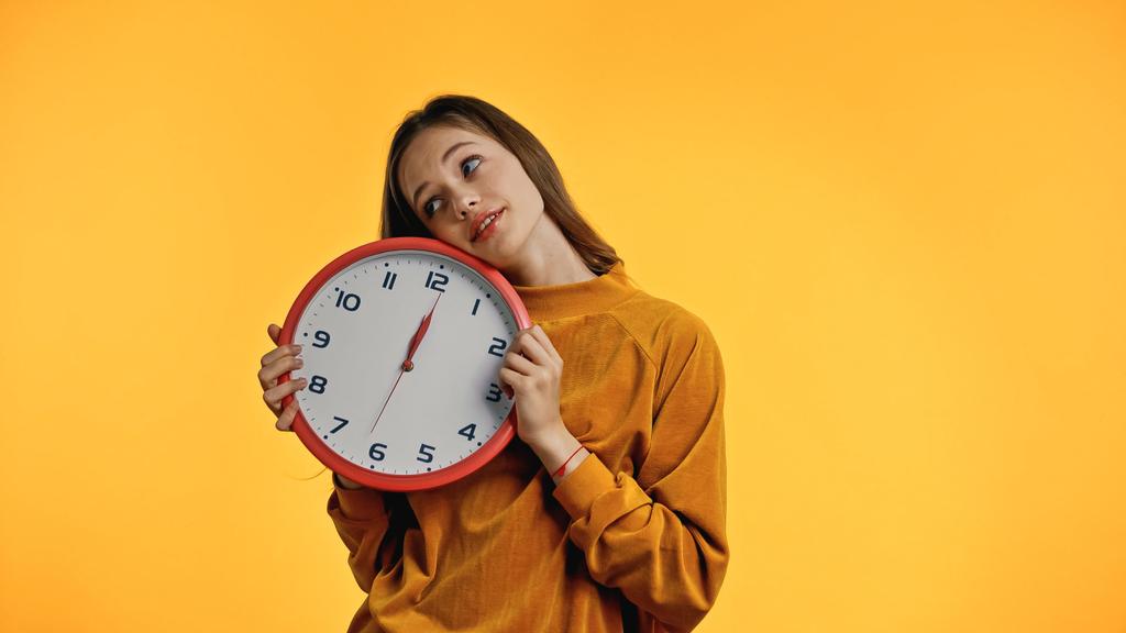 smiling teenager in sweater holding clock isolated on yellow - Photo, Image