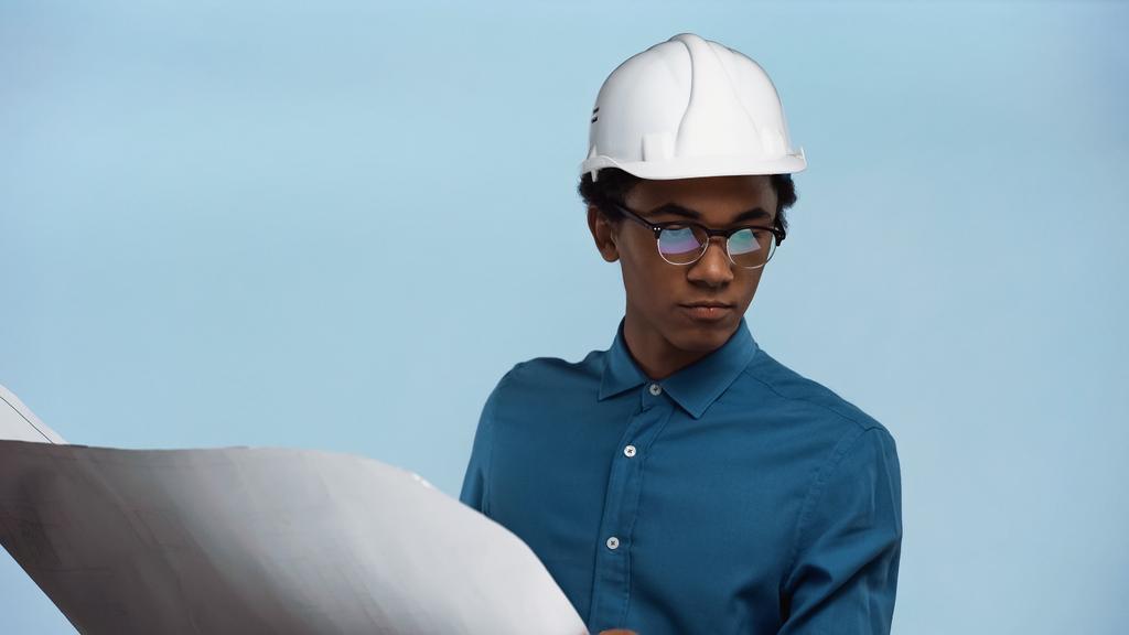africký americký dospívající chlapec v bezpečnostní přilbě drží modrotisk izolované na modré - Fotografie, Obrázek