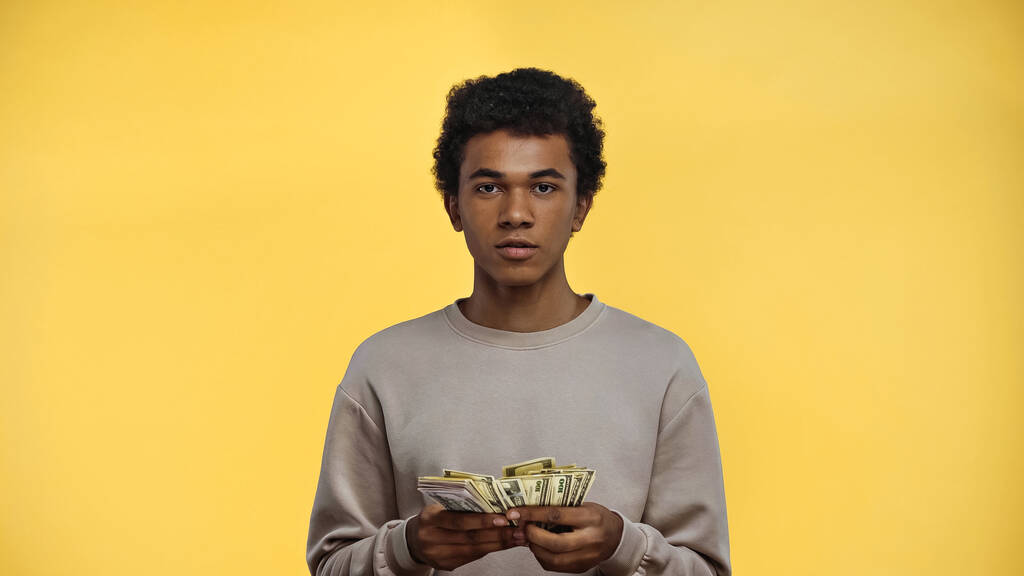 afrikanisch-amerikanischer Teenager im Sweatshirt mit Dollars auf gelbem Hintergrund - Foto, Bild