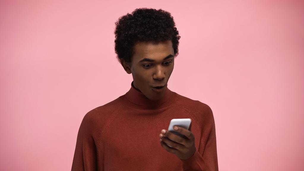 アフリカ系アメリカ人の10代の若者がピンクで隔絶されたスマートフォンを見て - 写真・画像