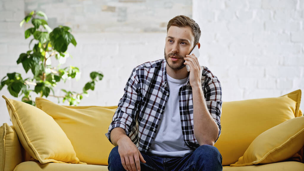 hombre barbudo hablando en el teléfono inteligente mientras está sentado en el sofá - Foto, imagen