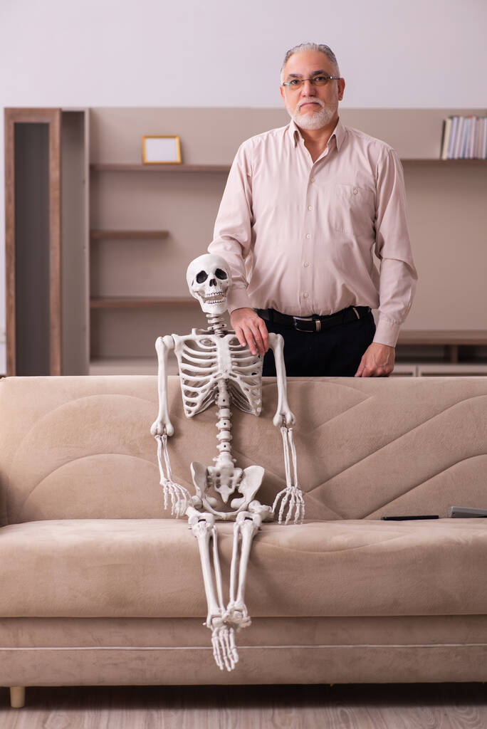 Vieil homme assis sur le canapé avec le squelette féminin - Photo, image