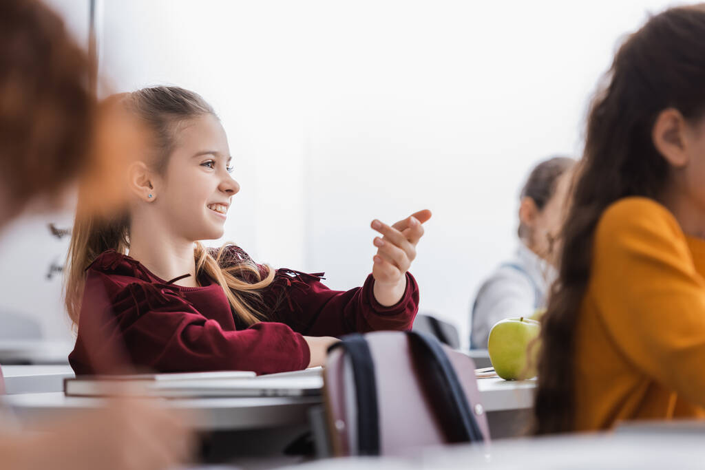 Pozitív tanuló ül közel alma, könyv és laptop elmosódott előtérben az osztályteremben  - Fotó, kép