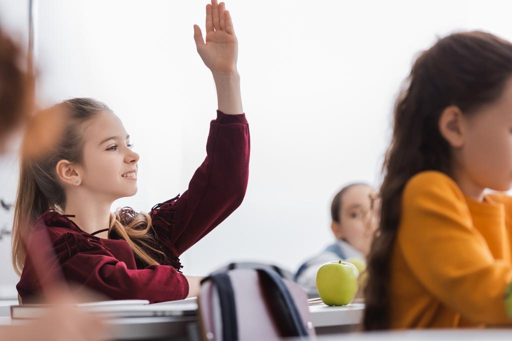 Hymyilevä koululainen nostaa kätensä lähelle omenaa ja kirjaa luokkahuoneessa  - Valokuva, kuva