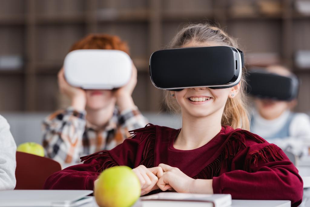 vrolijk meisje gaming in vr headset horen klasgenoten op wazig achtergrond - Foto, afbeelding