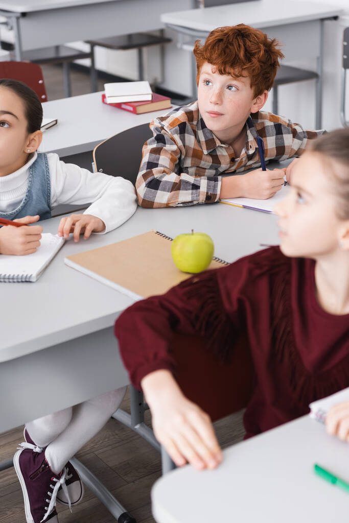 концентровані учні, які сидять за столами в класі під час уроку
 - Фото, зображення