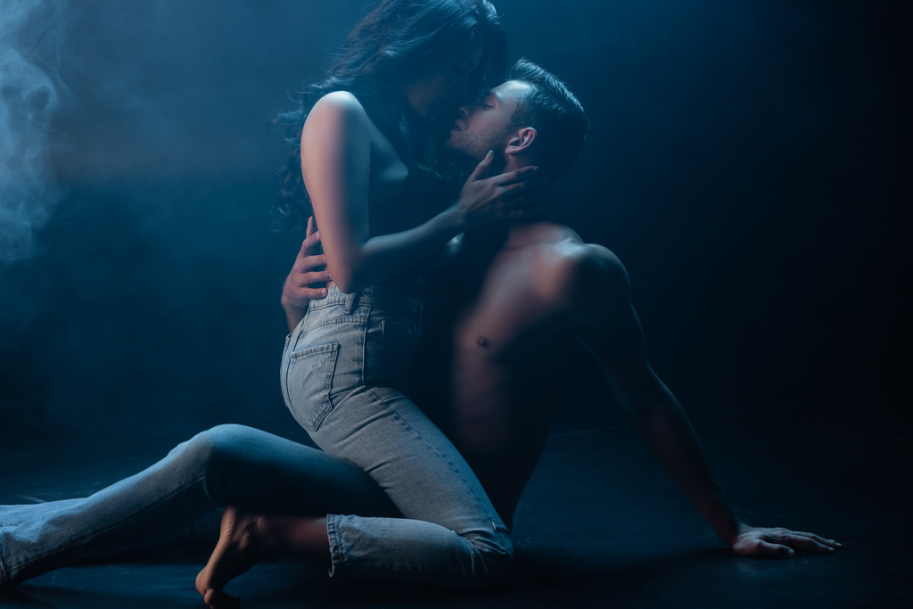 Sexy žena v džínách a podprsenka líbání přítel na černém pozadí s kouřem  - Fotografie, Obrázek